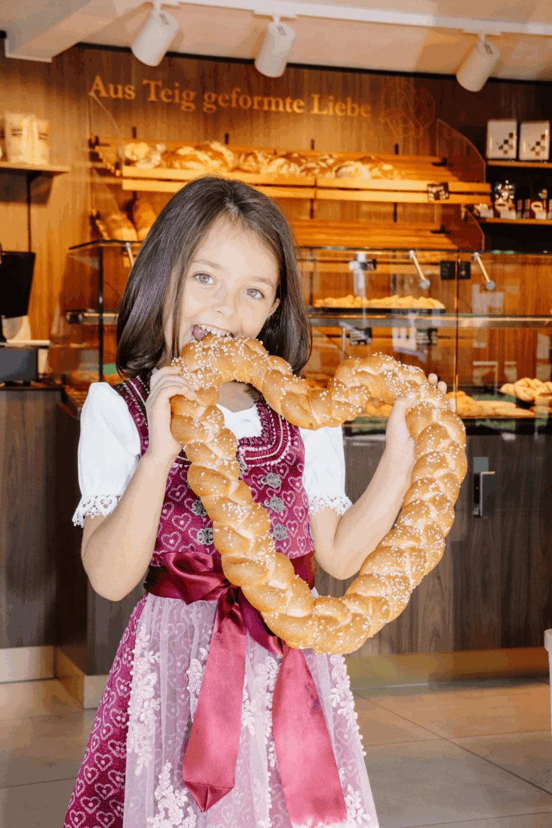 Ein kleines Mädchen beißt in eine riesige Breze als Herz.